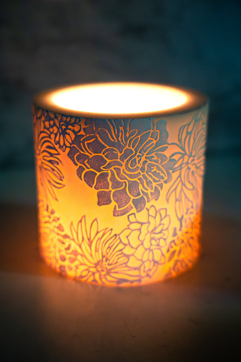 Decorative candle holder with floral patterns illuminated by a candle.